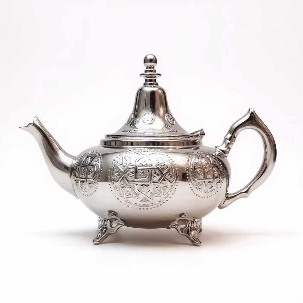 Hand-engraved Moroccan large teapot in polished silver on a white background, highlighting ornate spout, lid, and tripod feet.
