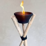 Handmade wooden tripod outdoor candle holder with black terracotta bowl and flame against neutral background