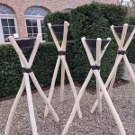 Set of four rustic wooden tripod candle holders arranged on gravel outdoor setting