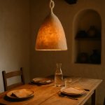 Beige wool lamp casting a warm halo over an intimate dinner table laid with minimalist stoneware in an adobe interior.