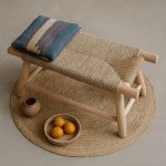 Handwoven straw bench with colorful striped pillow on round woven rug with decorative accents
