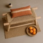 Handwoven straw bench styled with striped pillow, oranges, and bohemian decor on jute rug