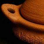 Close-up of hand-carved wheat pattern on rim of unglazed terracotta tagine pottery base and curved handle detail