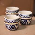 Close-up set of four blue espresso cups with lattice motifs on beige backdrop.