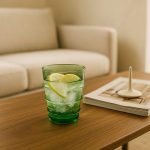 Emerald green glass tumbler with iced lemon water on wooden coffee table.