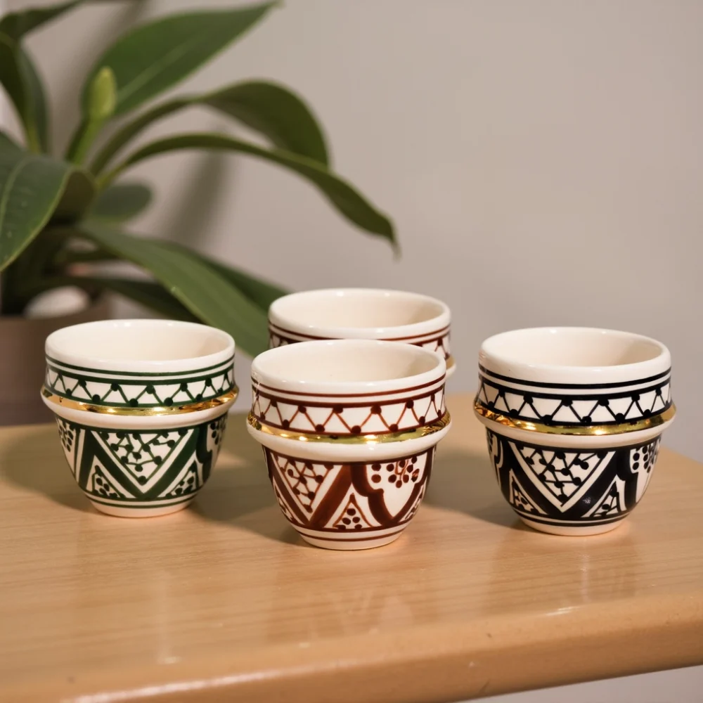 Four Moroccan espresso cups in green, amber, black, and blue geometric motifs with 24-k gold bands on wood shelf.