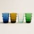 Four sapphire Moroccan glass tumblers (blue, amber, clear, green) showcased on a white backdrop.