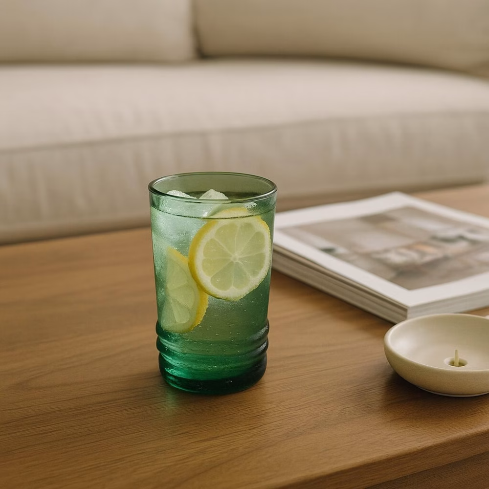 Green tumbler of iced lemonade on wood table in cozy neutral living room.