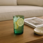 Green tumbler of iced lemonade on wood table in cozy neutral living room.