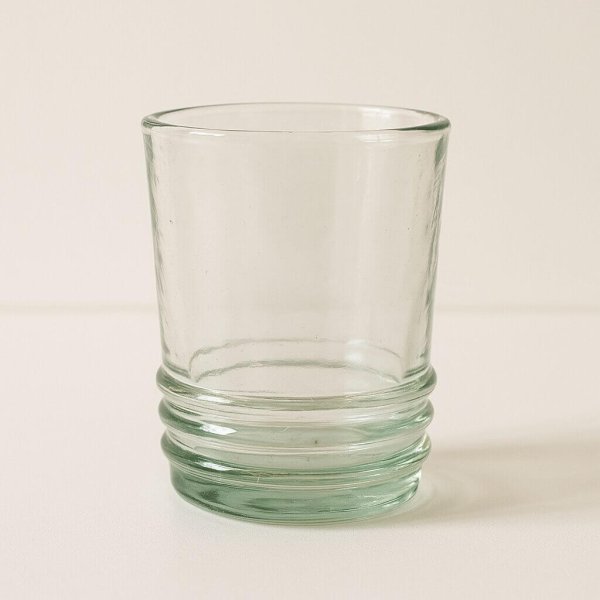 Isolated clear recycled glass tumbler against soft beige backdrop.