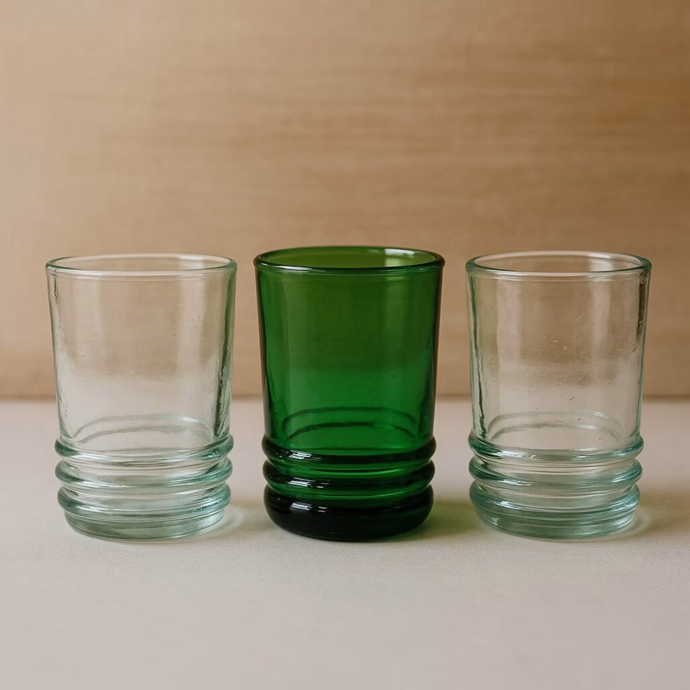 Row of three recycled glass tumblers—emerald flanked by two clear—in studio light.