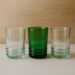 Row of three recycled glass tumblers—emerald flanked by two clear—in studio light.