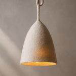 Side view of the suspended boiled-wool lamp with sculptural woolen cord against a neutral plastered wall.
