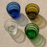 Stacked view of cobalt, amber, clear and emerald Moroccan glass tumblers against neutral cloth.