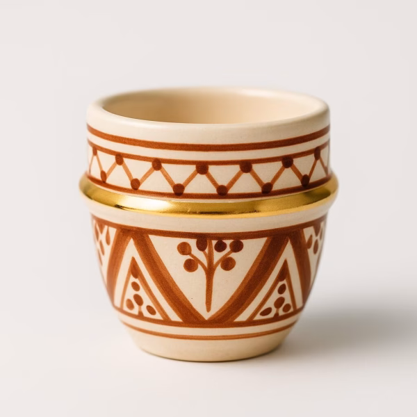 Studio shot of Moroccan espresso cup— terracotta patterns with gold bands— on a glossy white surface, reflected below.