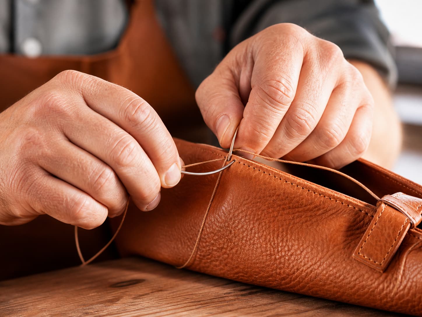 Close-up of artisan hands saddle-stitching a leather bag with waxed linen thread in a Marrakech workshop