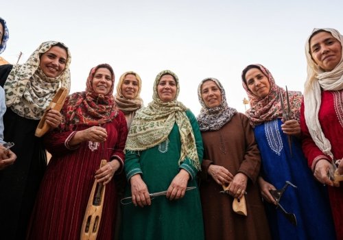 A low-angle group portrait of seven Beni Ourain rug weavers, smiling and holding their weaving tools, including shuttles and combs.