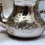 Close-up of hand-engraved silver teapot showing intricate floral medallion patterns and detailed craftsmanship