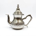 Hand-engraved silver teapot with ornate Moroccan medallion patterns and domed lid on white background