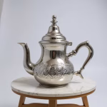 Studio shot of a medium hand‑engraved silver teapot on a small marble stool