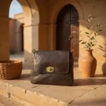 Handcrafted leather crossbody bag in Mediterranean courtyard setting with vintage brass hardware