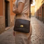 Woman wearing dark brown leather crossbody bag on cobblestone street showing adjustable strap