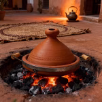 Unglazed terracotta tagine with handles cooking over open charcoal fire in authentic Moroccan courtyard
