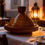 Traditional terracotta tagine pot with golden patterns on dinner table, Moroccan ceramic clay cooking vessel