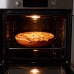 Oven-safe terracotta ceramic plate baking shepherd's pie in modern kitchen oven