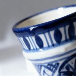 Close-up detail of handpainted ceramic espresso cup showing cobalt blue rim, glaze texture and geometric pattern