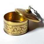 Brass decorative box with lid open showing smooth interior and hand-engraved exterior pattern