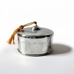 Hand-hammered silver decorative box with lid and gold tassel showing textured dimpled surface