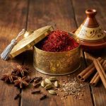 Brass decorative box with lid filled with saffron threads surrounded by cinnamon sticks and spices