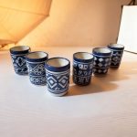 Six blue and white ceramic cups with geometric patterns displayed with warm ambient lighting