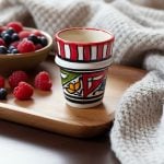 Handpainted ceramic espresso cup styled on wooden tray with fresh berries and cozy blanket