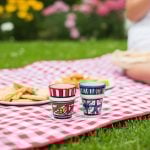 Two handpainted espresso cups on red gingham picnic blanket with cookies in outdoor setting
