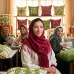 Hasna and her team of craftswomen in their embroidery workshop surrounded by colorful embroidered cushion covers displayed on shelves