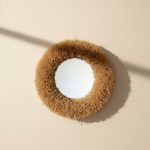 Overhead view of round handwoven straw mirror with thick plush raffia fringe showing circular artisan design