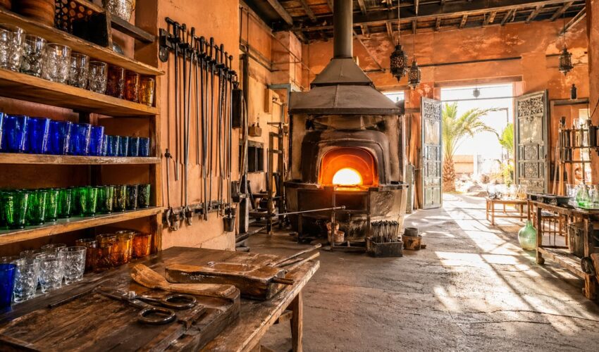 Younes's glassblowing workshop on Ourika Road, Marrakech — furnace, blowpipes, and rows of finished hand-blown glasses
