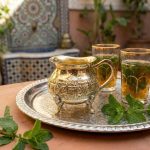Brass gold mini creamer pitcher on traditional silver serving tray with Moroccan mint tea glasses