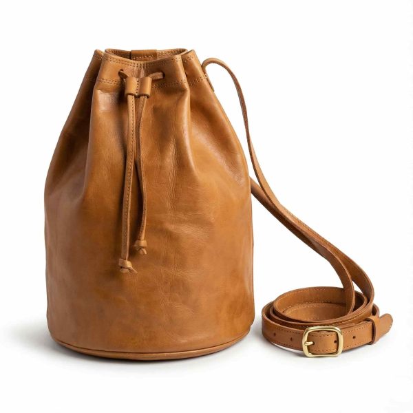Tan leather bucket bag front view with adjustable crossbody strap and brass buckle