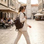 Woman wearing slim leather backpack walking through European city square