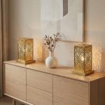 Perforated brass table lamps on modern oak sideboard casting warm ambient shadows alongside ceramic vase and dried flowers