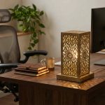 Hand-engraved brass accent lamp on executive wooden desk providing warm task lighting with leather journals and coffee mug