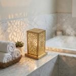 Hand-engraved brass accent lamp on marble bathroom counter creating ambient spa lighting with rolled towels and succulent