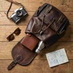 Flat lay of leather backpack with travel essentials camera passport wallet