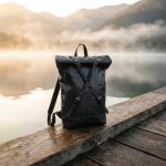 Black leather roll top backpack on wooden dock at misty mountain lake