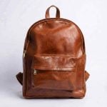 Minimalist leather backpack in tan brown featuring a front zippered pocket and brass hardware, handcrafted from full-grain Moroccan leather