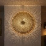 Brass filigree wall lamp mounted on textured white wall projecting warm geometric light patterns