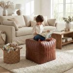 Child reading book while sitting on brown leather cube ottoman in cozy neutral living room